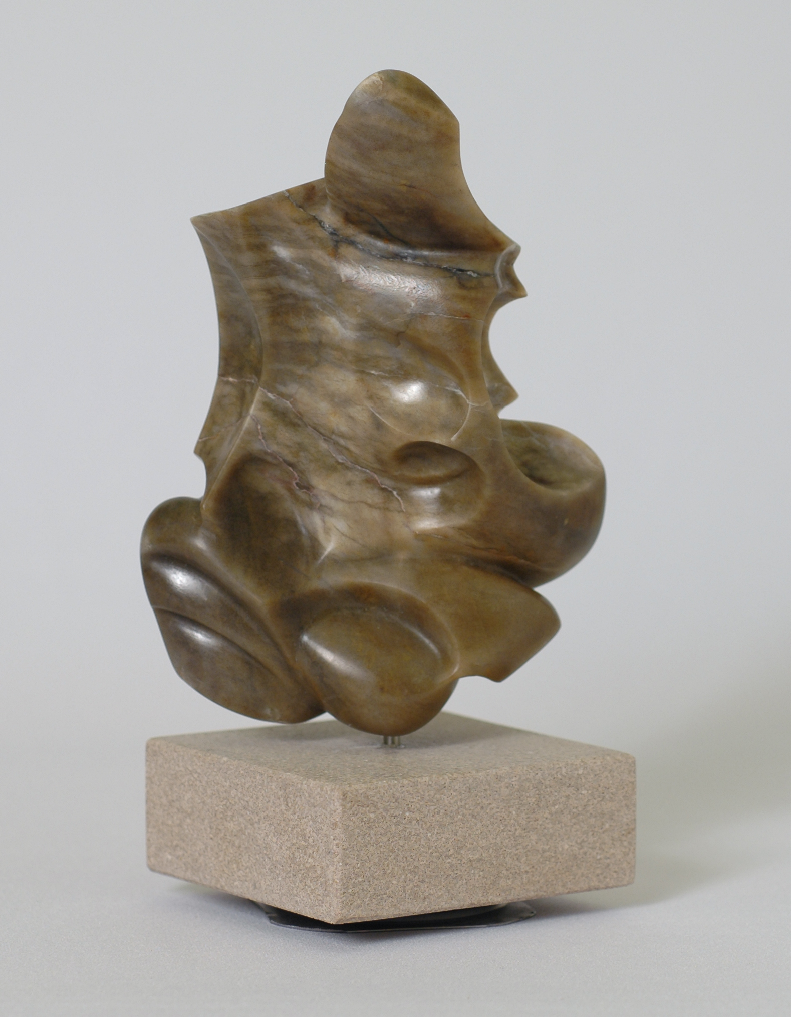 Abstract sculpture in brown stone with rounded, overlapping organic forms, set on a beige stone base.