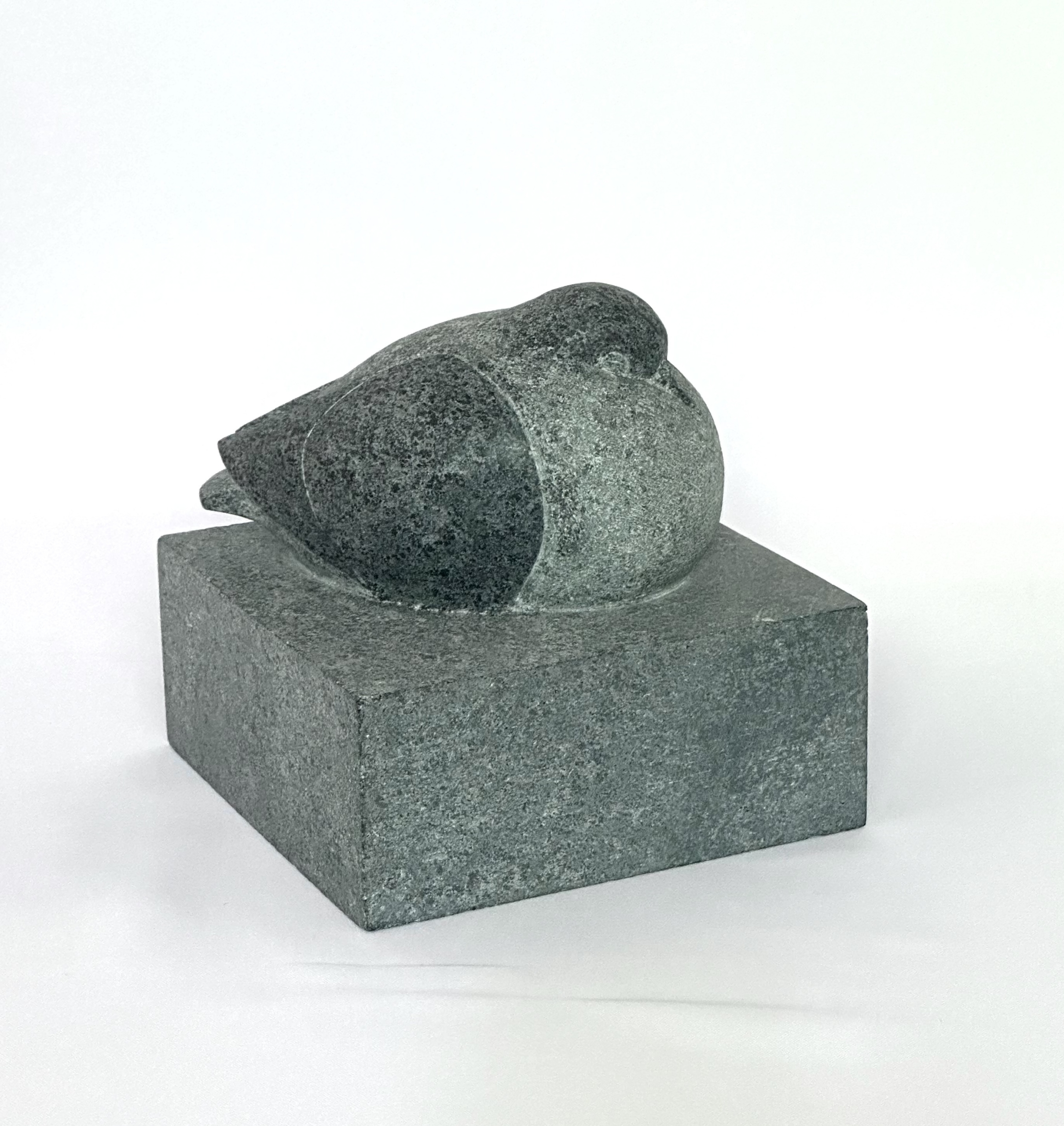 Smooth grey soapstone sculpture of a curled, sleeping pigeon, resting on a matching grey stone cube base.