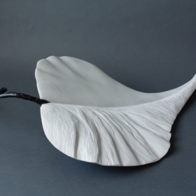 Vent-dautomne_1 White marble sculpture in the shape of a leaf, with a black stem evoking a twig.