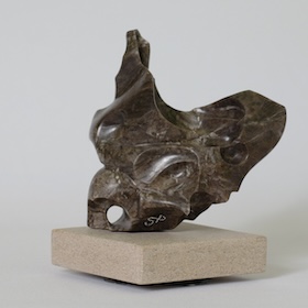 Abstract sculpture in dark grey-brown stone with a small round opening, set on a beige stone base.