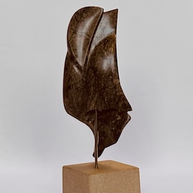 vent-dans-les-voiles-thumbnail Abstract dark brown stone sculpture resembling a stylized sail, mounted on a thin rod atop a beige stone base.